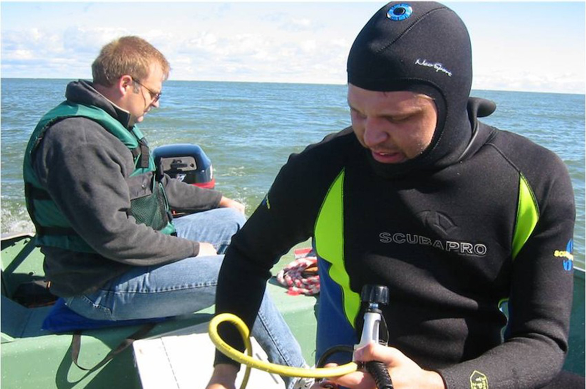 Man in wet suit holding SCUBA regulator